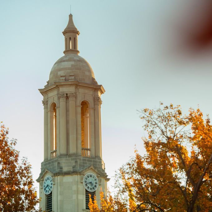 A white stone clock tower softly lit with tree leaves in the foreground turning brown and orange
