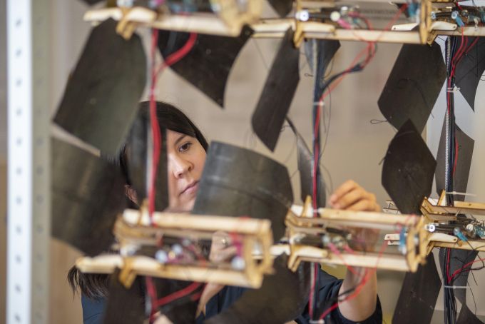 A woman with black hair stands adjusting back curved panels on a  dynamic window-shading system