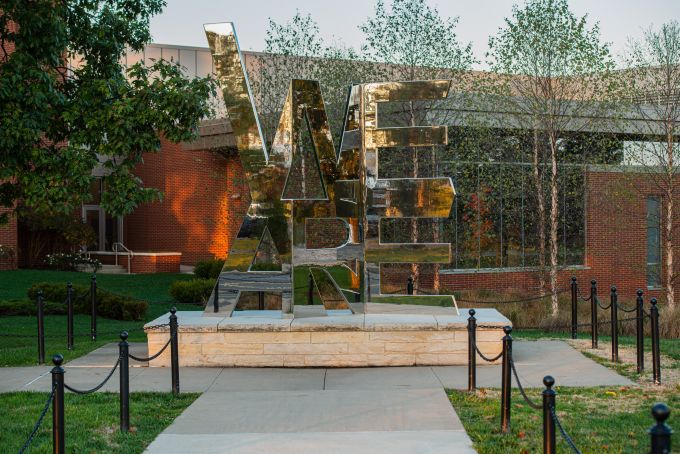 Shiny stainless sculpture that reads We Are reflects fall foliage colors on its surface